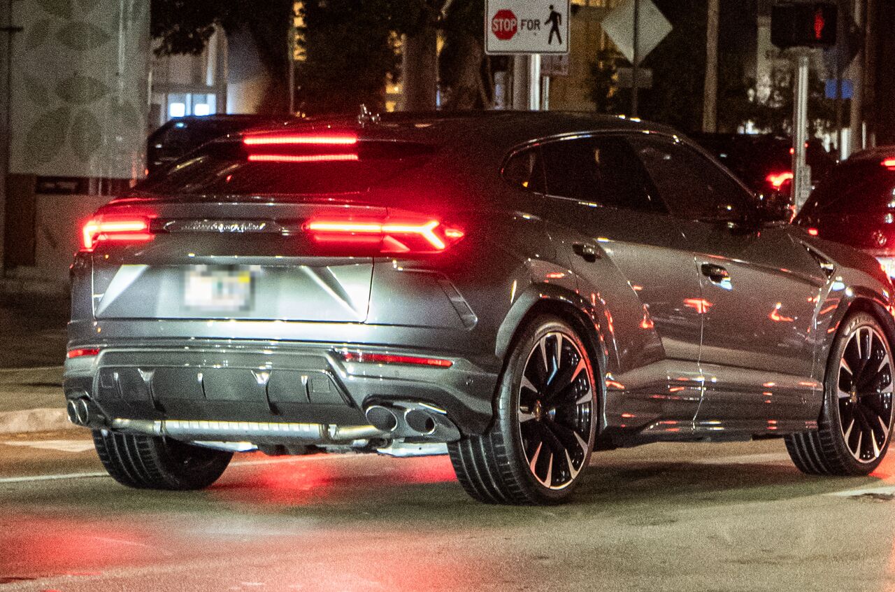 Traseira de um Lamborghini Urus cinza parado numa esquina à noite, com as lanternas vermelhas acesas